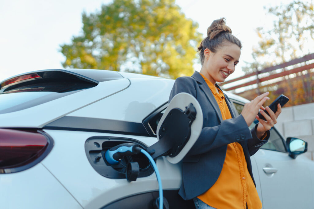 Photograph of a person using her phone while charging an electric vehicle